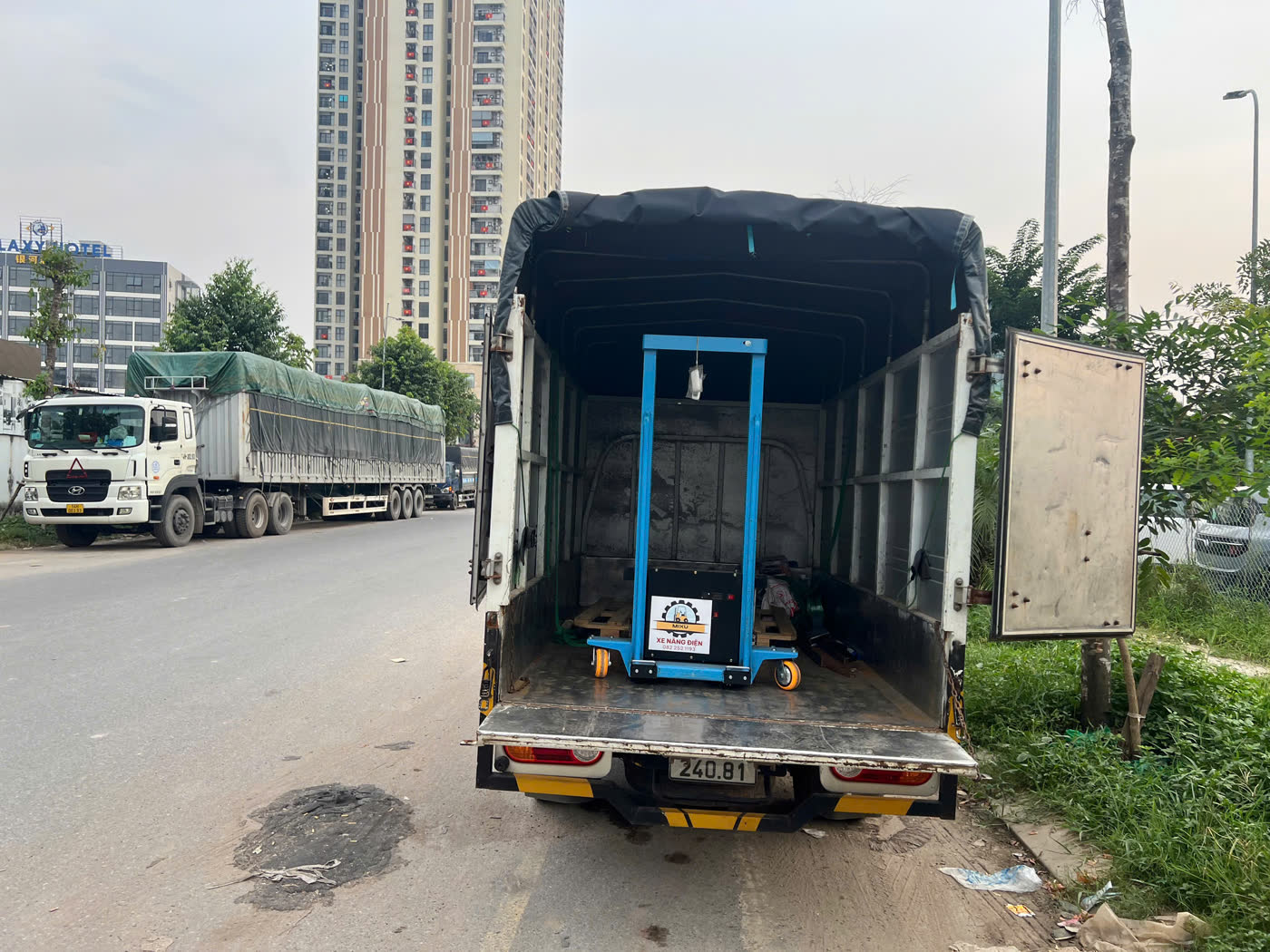 Xe nâng MIXU màu xanh đứng gọn trong thùng xe tải giữa khu đô thị