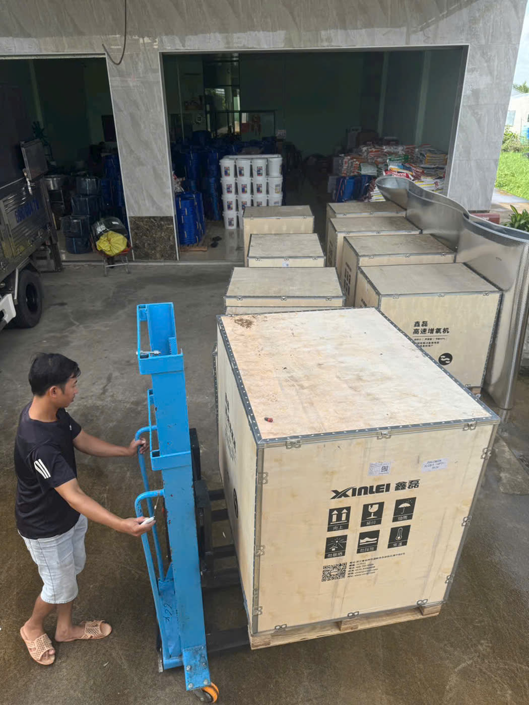 Một người dùng xe nâng MIXU màu xanh xếp kiện máy gỗ trước kho