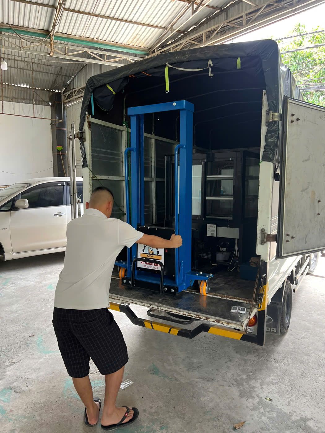 Xe nâng MIXU màu xanh đã lên thùng xe tải, tài xế đẩy vào trong