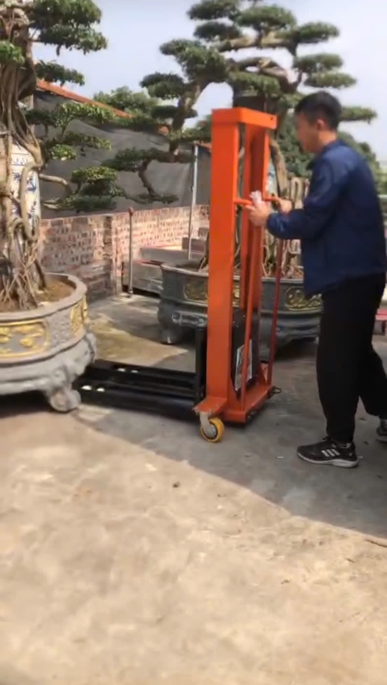 Một người nâng chậu bonsai đá nặng bằng xe nâng MIXU màu cam
