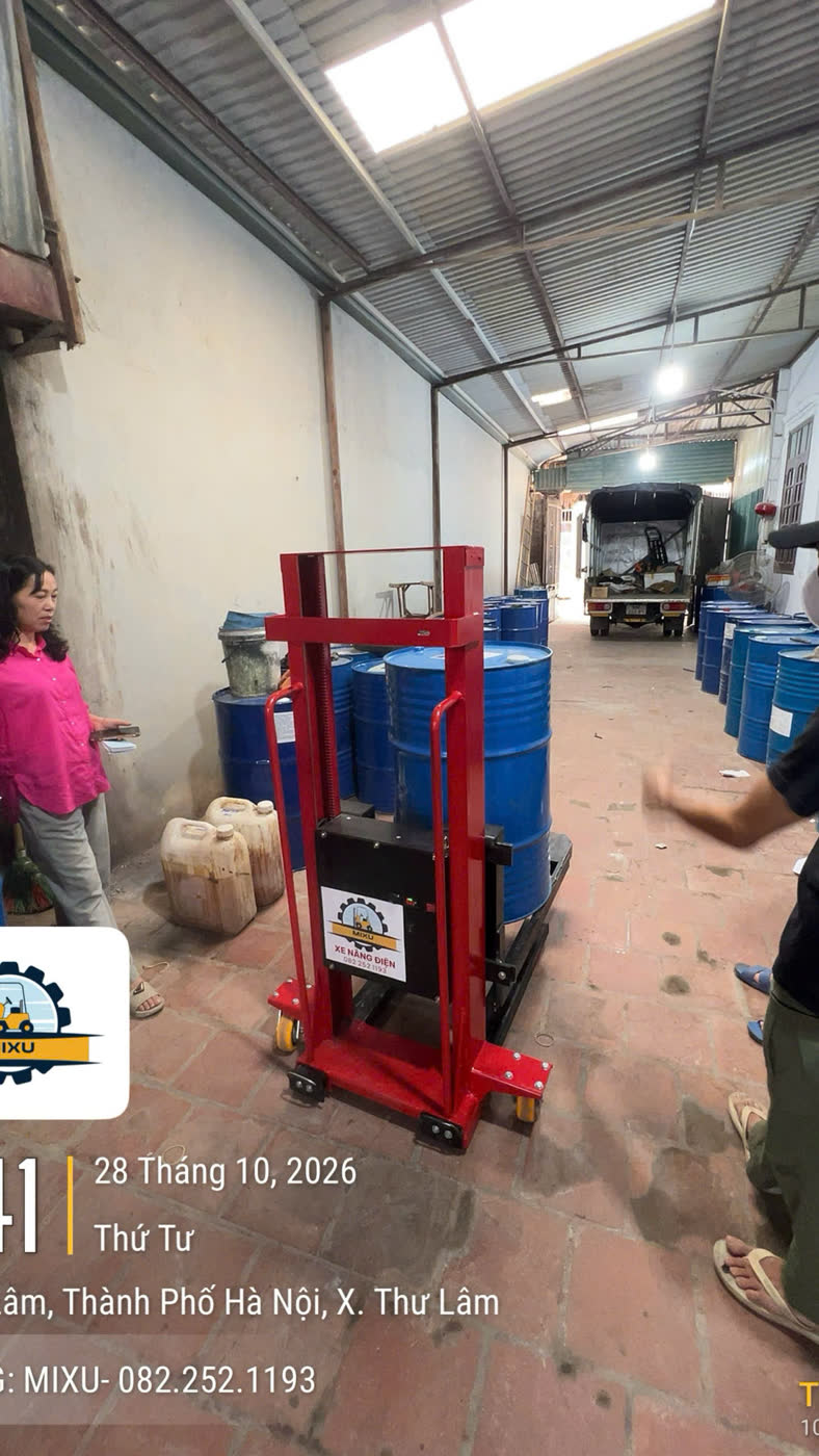 Xe nâng MIXU trong lối đi hẹp giữa các thùng phuy dầu, xe tải ở cuối lối